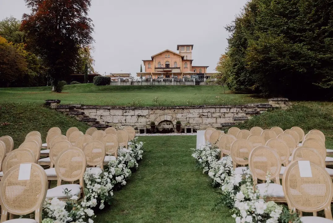 Stuhlreihen und weiße Blumen am Gang einer freien Trauung im Park vor einer Villa