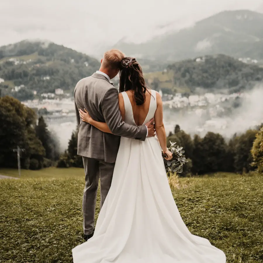 Brautpaar Arm in Arm auf einer Bergwiese mit Blick auf die Alpen